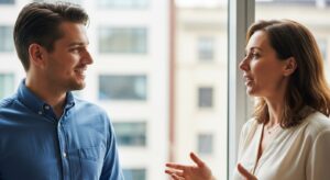 二人の同僚が向かい合って話す。 一人は相手の話にうなずきながら微笑み、真剣に耳を傾けている。 「傾聴・共感・安心感」を象徴する構図。