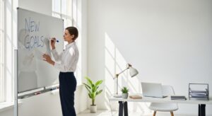 明るいオフィスでホワイトボードに新しい目標を書く人物。再スタートを象徴する構図。